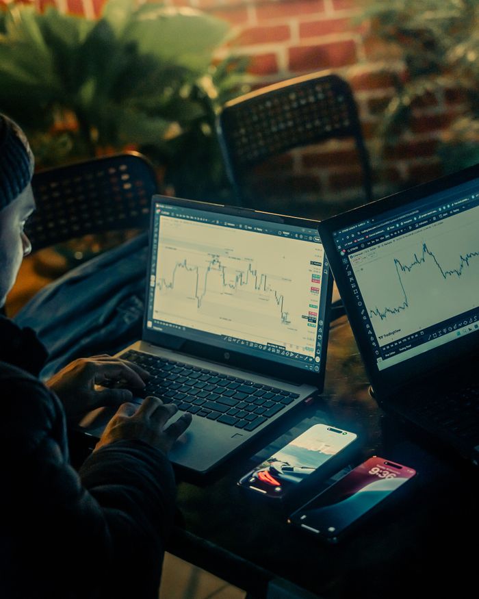 Person analyzing stock market data on laptops and smartphone outdoors at night.